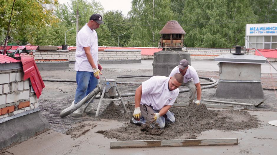 Construction workers applying roofing material on flat roof surface